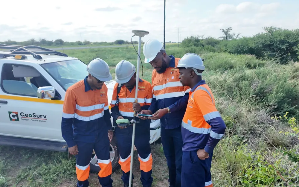 Four GeoSurv surveyors gathered around a GNSS receiver pole in the field