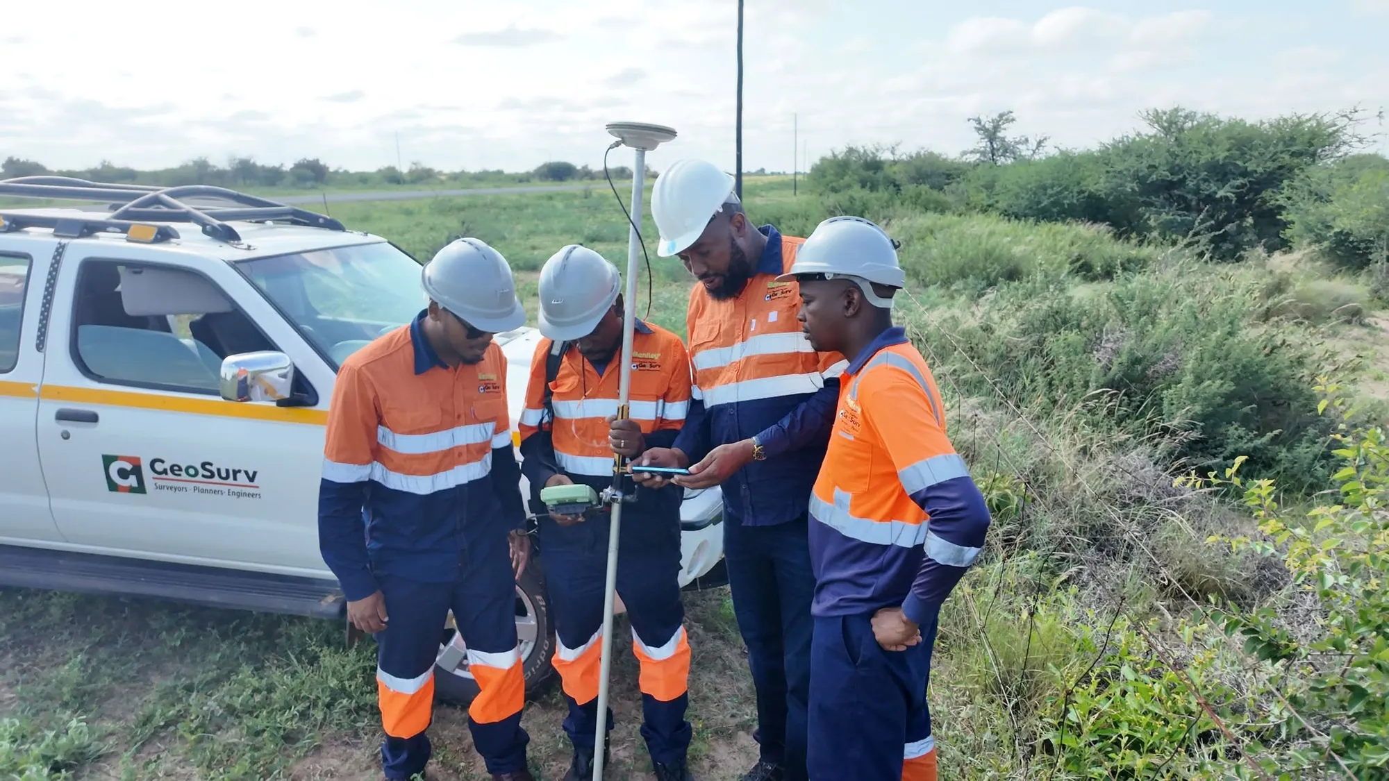 GeoSurv surveyors gathered around a GNSS receiver pole in the field in Botswana