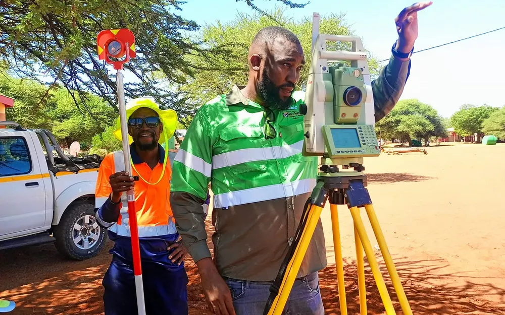 GeoSurv surveyor at a total station with a colleague holding a prism pole