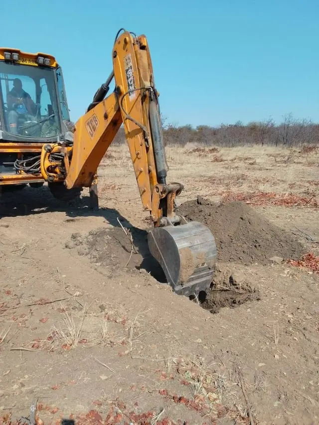 Yellow excavator digging a pit on cleared bushland